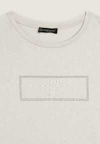 T-shirt grigio chiaro a maniche corte con scollo rotondo. Presenta una toppa logo testurizzata e decorata con strass al centro.