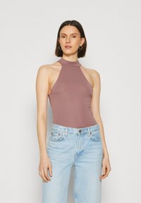 Světle mauve body s vysokým límcem a bezrukávovým střihem, spárované se světle modrými džíny. Hladká textilie a přiléhavý silueta.