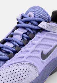 Scarpa sportiva viola con tomaia in mesh, motivo testurizzato, accenti grigio scuro e lacci coordinati. Logo Nike ben visibile e collare imbottito.