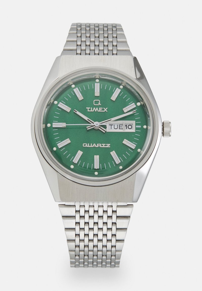 Reloj de cuarzo Timex con un dial verde, marcadores de hora en tono plateado y una pantalla de fecha. Presenta una pulsera de malla de acero inoxidable y una caja hexagonal.