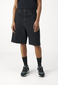 Svarte denimshorts med løs passform, med knappelukking og sidelommer. Kombinert med svarte sokker til kneet og joggesko.