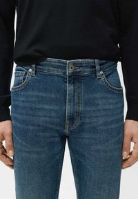 Tummansininen denim-farkut slim fit -leikkauksella, joissa on perinteinen viiden taskun muotoilu ja hienovarainen haalistuma edessä. Metallinen nappikiinnitys.