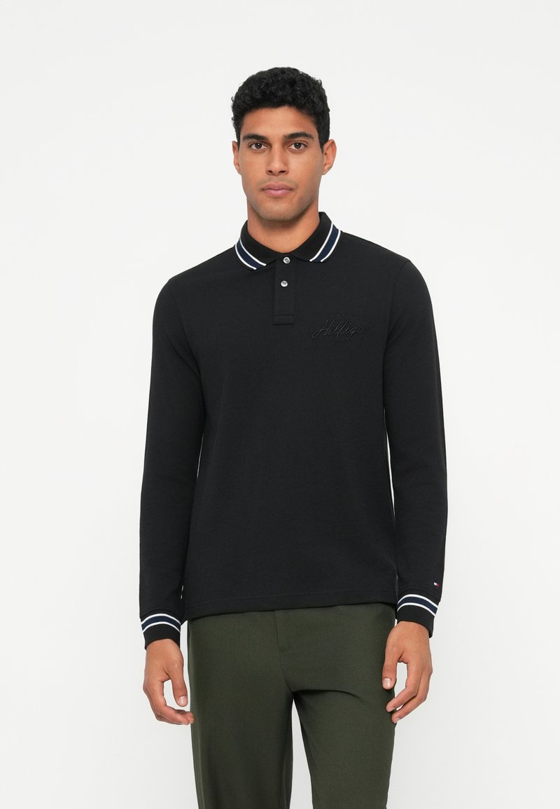 Melnas garām piedurknēm polo krekls ar apkakli, ar baltām svītrām apkaklē un piedurknēs, ar izšūtu logotipu uz krūškurvja.