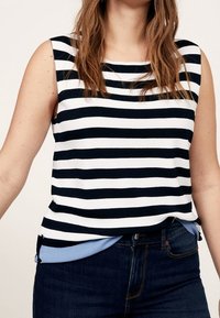 Mouwloos top met marineblauwe en witte horizontale strepen, gemaakt van een zachte stof. De onderste laag in lichtblauw piept onder de zoom vandaan.