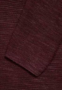 Close-up van een gevouwen mouw waarin de geribbelde breimateriaal van donker burgundy stof zichtbaar is.