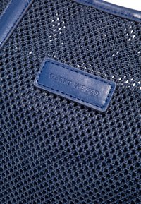 Marineblaues Netzhandtasche mit Lederakzenten, ausgestattet mit einem rechteckigen Lederetikett, das mit "GERRY WEBER" geprägt ist. Strukturierter und atmungsaktiver Entwurf.