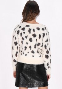 Paita fuzzy berwarna krim dengan pola leopard berwarna coklat tua, dilengkapi dengan leher bulat dan tepian bergaris. Dipadukan dengan rok kulit hitam yang ramping.