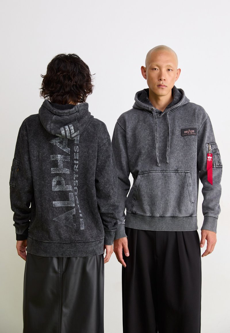Dunkelgrauer Kapuzenpullover in einem verblassten Finish. Mit Logo auf dem Rücken, Kängurutasche, Seitentasche mit Reißverschluss und roten Akzentdetails.