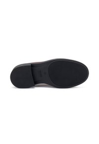 Suola in gomma nera di una scarpa con superficie texture, caratterizzata da un tacco leggermente rialzato e un'impronta del logo vicino all'area del tallone.