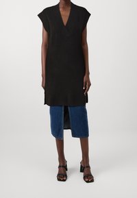 Abito senza maniche in maglia nera con scollo a V, abbinato a una gonna di denim con uno spacco frontale, indossato con sandali neri con tacco a blocco.