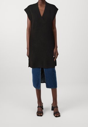 Zwarte gebreide mouwloze jurk met een V-hals, gecombineerd met een denim rok met een split aan de voorkant, gedragen met zwarte blokhak sandalen.