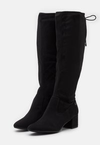 Mustat mokkasaappaat, joissa on korkea varsi, terävä kärki, paksu korko, joustavat sivupaneelit ja sivuvedin helppoa pukeutumista varten.