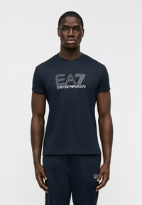 Κοντομάνικο μπλουζάκι σε ναυτικό μπλε χρώμα, κατασκευασμένο από βαμβάκι, με λευκό κεντημένο λογότυπο της μάρκας "EA7 Emporio Armani" στο στήθος.