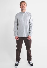 Chemise à manches longues gris avec une texture subtile, associée à un pantalon marron. Des baskets noir et blanc complètent la tenue.