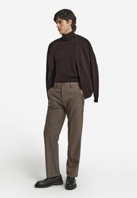 Brązowy golf w połączeniu z ciemnobrązowym kardiganem, jasnobrązowymi spodniami w kratę oraz czarnymi skórzanymi butami. Prosty, nowoczesny design.