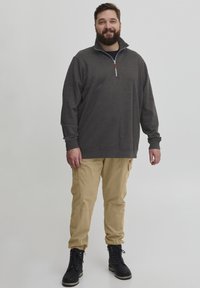 Grau zip-up Pullover mit hohem Kragen, kombiniert mit beigen Cargo-Hosen und schwarzen Schnürstiefeln. Der Pullover hat eine Lederakzent.