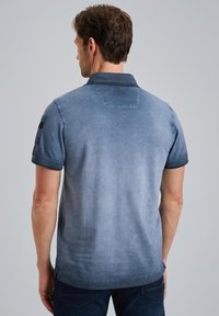 Polo shirt blu con una sfumatura degradante, maniche corte e colletto. Presenta una toppa sulla manica sinistra e dettagli di cucitura lungo i bordi.