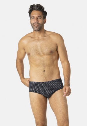 Slip de bain pour hommes en bleu marine avec un motif à pois blancs, présentant une coupe ajustée et un tissu lisse, offrant un style contemporain.