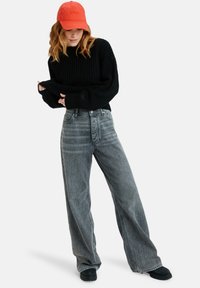 Black ribbed knit sweater, high-waisted gray wide-leg jeans, and an orange cap. Soft texture, relaxed fit, with stitching and button details.