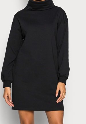 Robe noire à manches longues en tissu doux ; présente un col montant et une coupe décontractée, arrivant au-dessus des genoux avec des poignets côtelés.