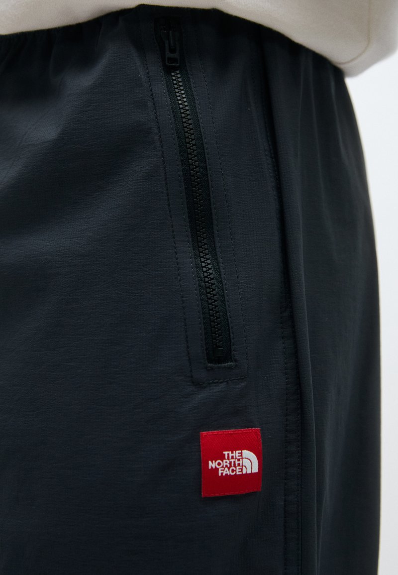 Svarta tygbyxor korta som har en sidoficka med dragkedja och en röd rektangulär logotyp patch från The North Face. Slät textur.