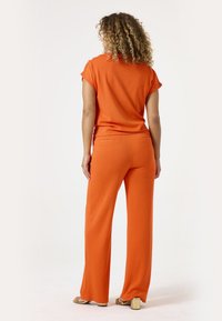 Oranje twee-delige outfit bestaande uit een kortrokende top en wijde broek, gemaakt van een gladde stof met een ontspannen pasvorm en subtiele stikdetails.