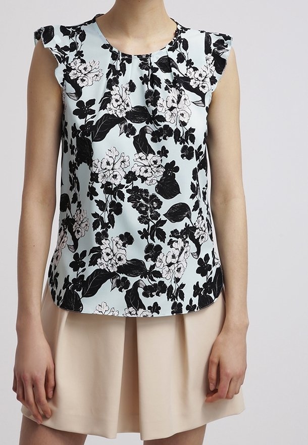 Canotta azzurro chiaro con stampa floreale nera e bianca, spalle arricciate, indossata con una gonna plissettata beige.