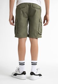 Shorts cargo verts avec deux poches latérales, des poches arrière et une coupe droite. Portés avec des chaussettes blanches ornées de rayures noires et des baskets.