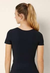 Maglietta nera aderente a maniche corte con scollo rotondo, texture liscia e silhouette sartoriale, vista da dietro.