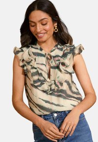 Blusa senza maniche in beige chiaro con scollatura arricciata, motivo a righe verdi e rosa e dettaglio con fiocco davanti. Tessuto morbido.
