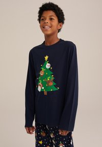 Mornarsko srajco z dolgimi rokavi z grafičnim dizajnom božične smrečice, ki vključuje okraske in luči; v kombinaciji z vzorčastimi pižamami.