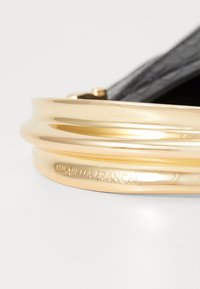 Gold-tone metal bracelet with a smooth curved design and embossed "ELISABETTA FRANCHI" text, set against a textured black background.