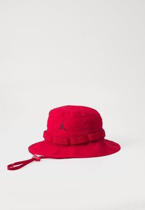 Czerwony kapelusz typu bucket z czarnym logo Jumpman, regulowany pasek na koronie oraz czerwony pasek pod brodą z zaciskiem na białym tle.