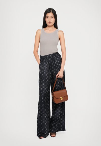 Graues, geripptes Tanktop, marineblaue, weit geschnittene Hose mit Muster und goldenen Akzenten, braune Handtasche mit Verschluss und Open-Toe-Absätze. Modell posiert mit den Händen in den Taschen.