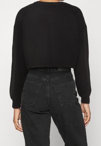 Felpa nera corta con maniche lunghe, scollo tondo e polsini a coste. Abbinata a jeans neri a vita alta con tasche posteriori.