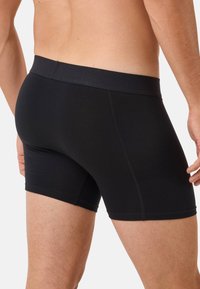 Male torso and upper legs wearing black fitted boxer briefs, showing back and side details against plain light background.