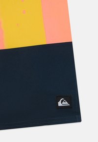 Mnohofarebná látka s ružovými, žltými a námorníckymi sekciami. Obsahuje čiernu nášivku s logom a grafikou hory na spodnej časti.