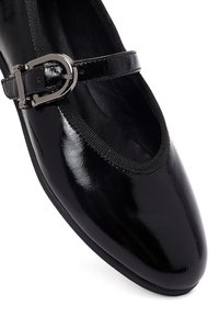 Zapato Mary Jane de charol negro con punta redondeada, correa elástica y acento con hebilla plateada. Textura lisa y brillante.