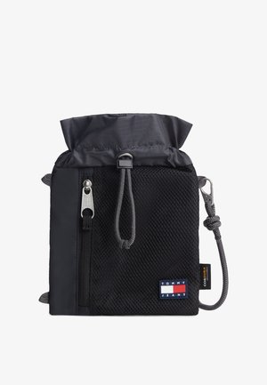 Czarna sakiewka Tommy Jeans z troczkiem, z przednią kieszenią z siateczki, zamkiem błyskawicznym, szarym paskiem sznurkowym z metalowym klipsem oraz etykietą z tkaniny Cordura.