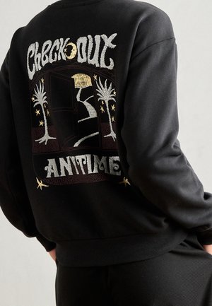 Zwarte sweatshirt met geborduurd ontwerp van een open deur, palmbomen en sterren, met de tekst "Check Out Anytime" op de achterkant.