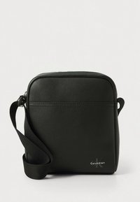 Juoda odinė per petį nešiojama rankinė su užtrauktuku, reguliuojama medžiagine rankena ir iškaltu Calvin Klein logotipu priekyje.