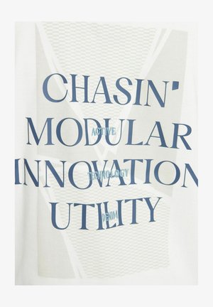 Vitt tyg med djärv blå text som stavar "CHASIN' MODULAR INNOVATION UTILITY ACTIVE TECHNOLOGY DENIM", med ett lager av grafiskt mönster.