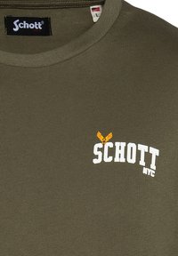 Camiseta de color verde oliva hecha de algodón, con cuello redondo, mangas cortas y un logo blanco con un acento naranja. Textura suave.