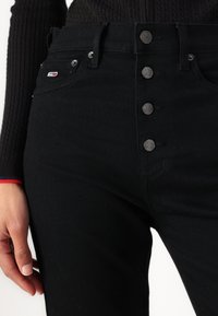 Sorte høytlivsjeans laget av denim. Har fem metallknapper og et lite logopatch. Glatt tekstur med en tettsittende fasong.