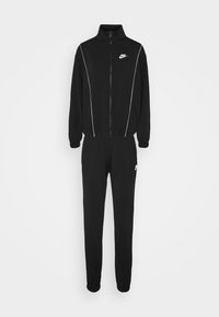 Tuta Nike nera con giacca zip e piping bianco, accompagnata da un paio di pantaloni abbinati. Il materiale è morbido, progettato per il comfort.