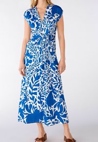 Robe maxi en bleu et blanc, présentant un motif floral, un détail de nœud à la taille, des manches courtes et une texture de tissu lisse.
