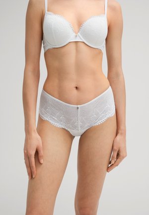 Witte kant beha en bijpassende short met gedetailleerde bloemmotieven, geschulpte randen en een soepele textuur. Verfraaid met een klein sieraad.