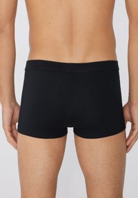 Boxers en coton noir avec une taille douce, présentant une coupe ajustée et une texture lisse, présentés de dos.
