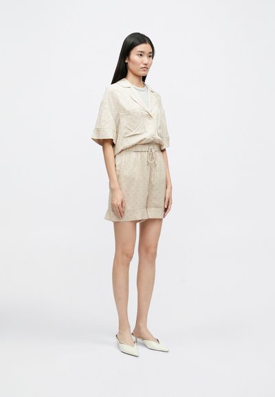 Béžová krátka súprava, ktorá obsahuje košeľu s golierom a prednou vreckom spolu s kraťasmi na šnúrku. Hladká textúra s jemným mriežkovým vzorom.