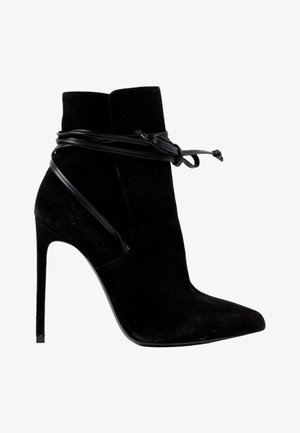 Bottine noire en daim à talon haut avec bout pointu et fins lacets en cuir enroulés autour et noués à l'avant.
